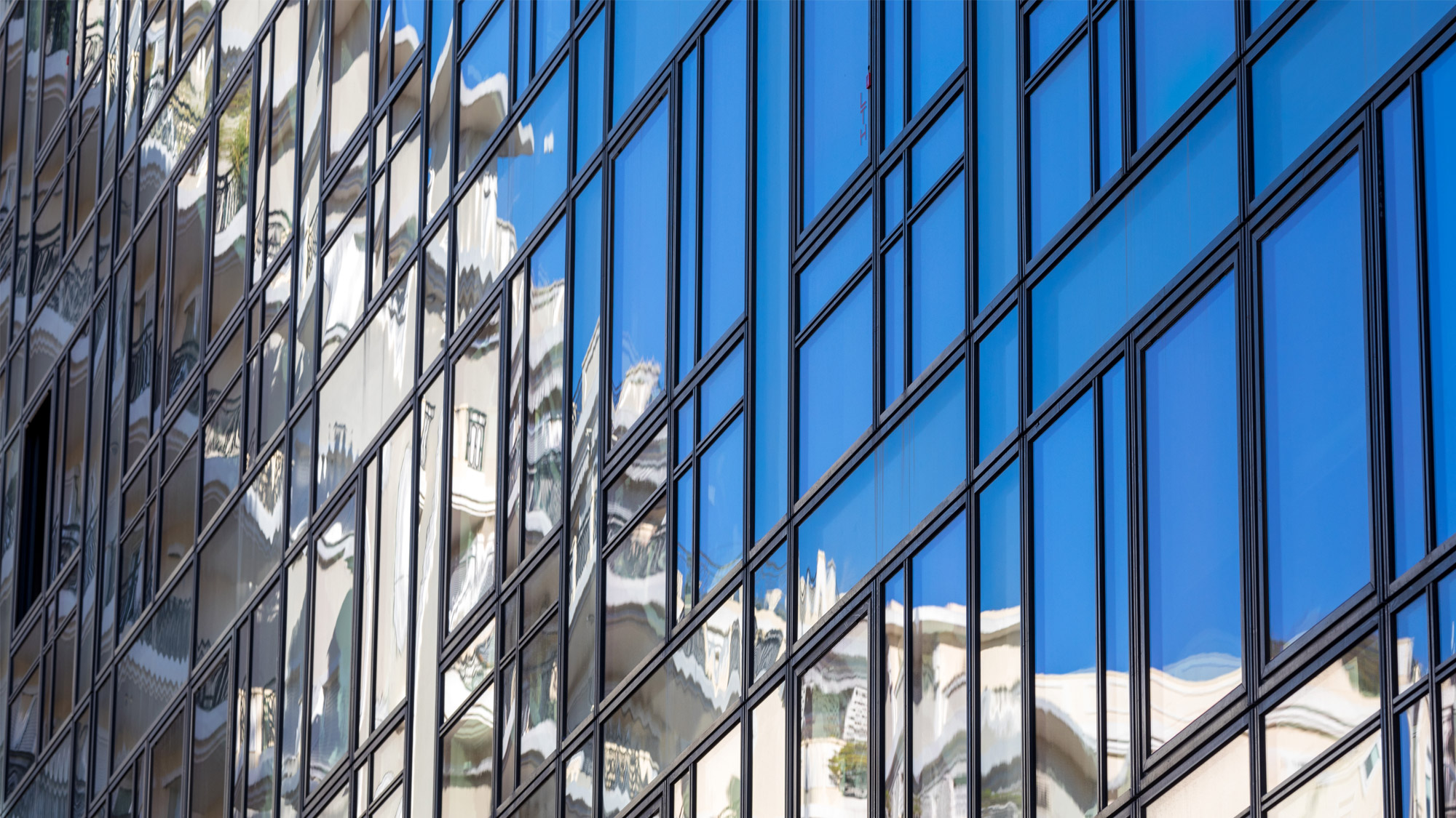 Une facade en verre d'un immeuble a monaco avec une reflection du ciel